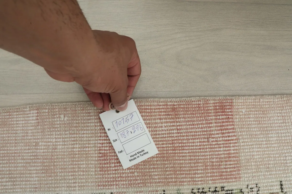 Hand holding a tag showing the rug's unique number and dimensions, confirming its origin