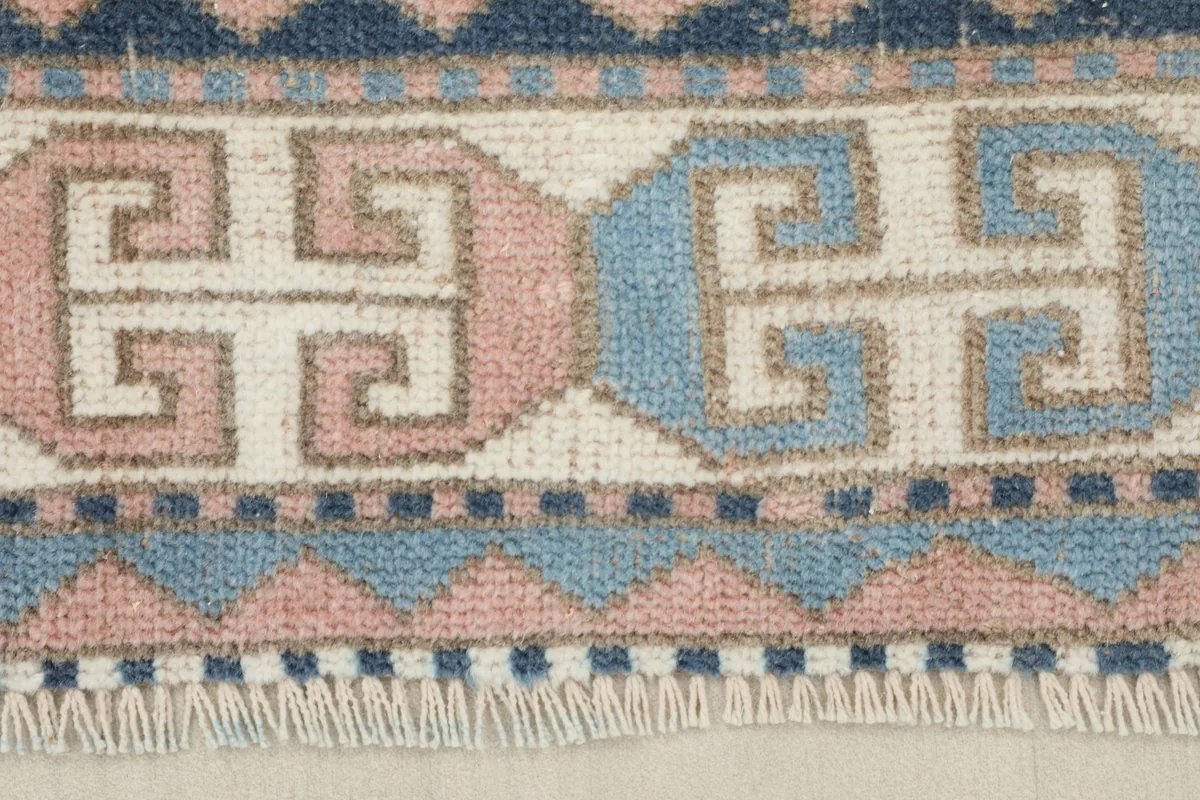 Close-up of the rug's geometric border design in navy, blue, rose, and ivory with short fringes.