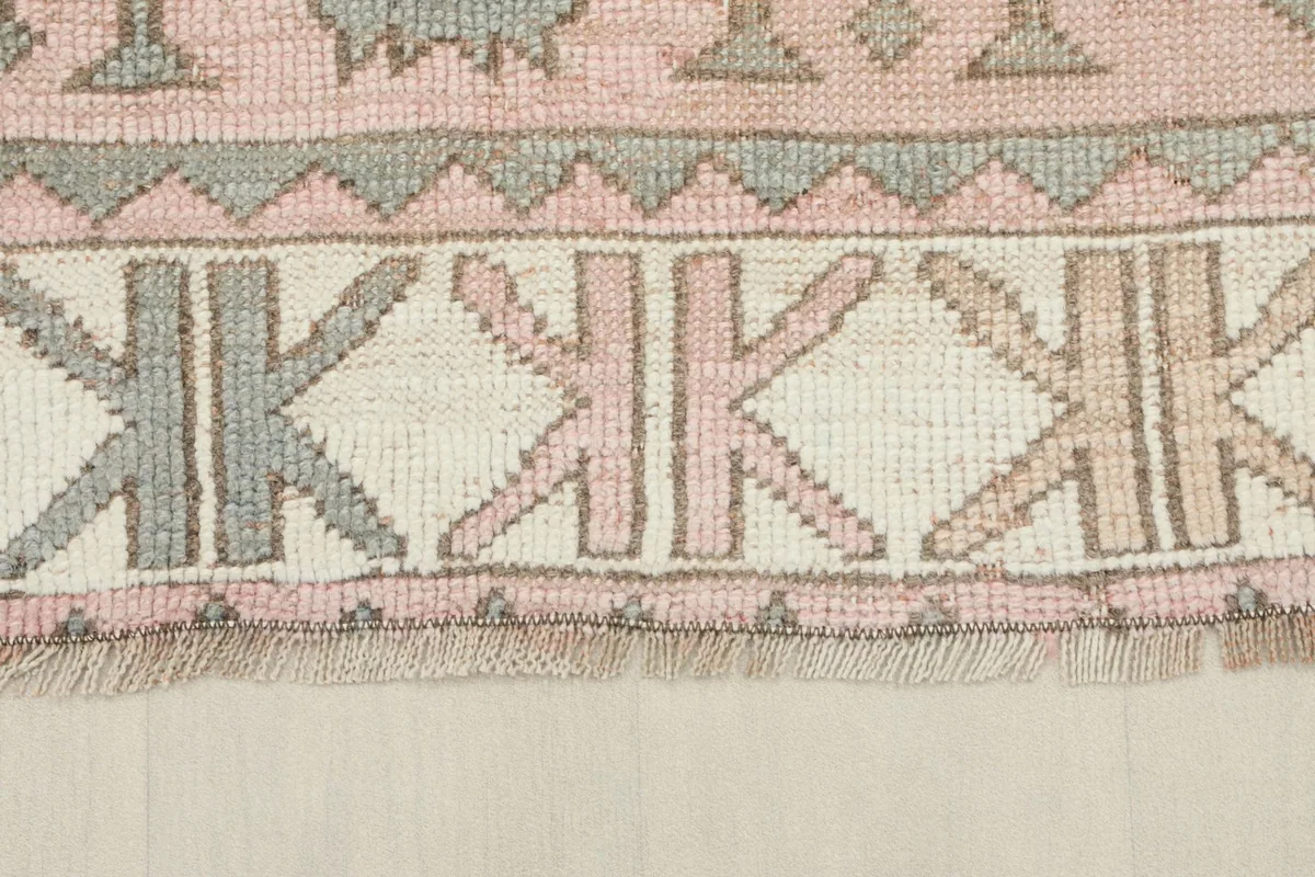 Detailed view of the rug's border design, featuring geometric patterns in ivory, rose, and gray.