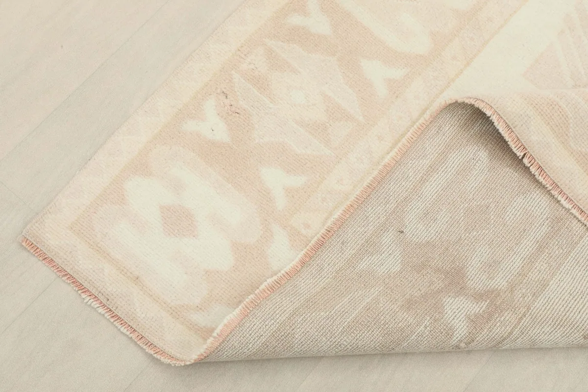 Corner of the rug folded back to show the cotton foundation and the reverse side of the hand-knotted pile.