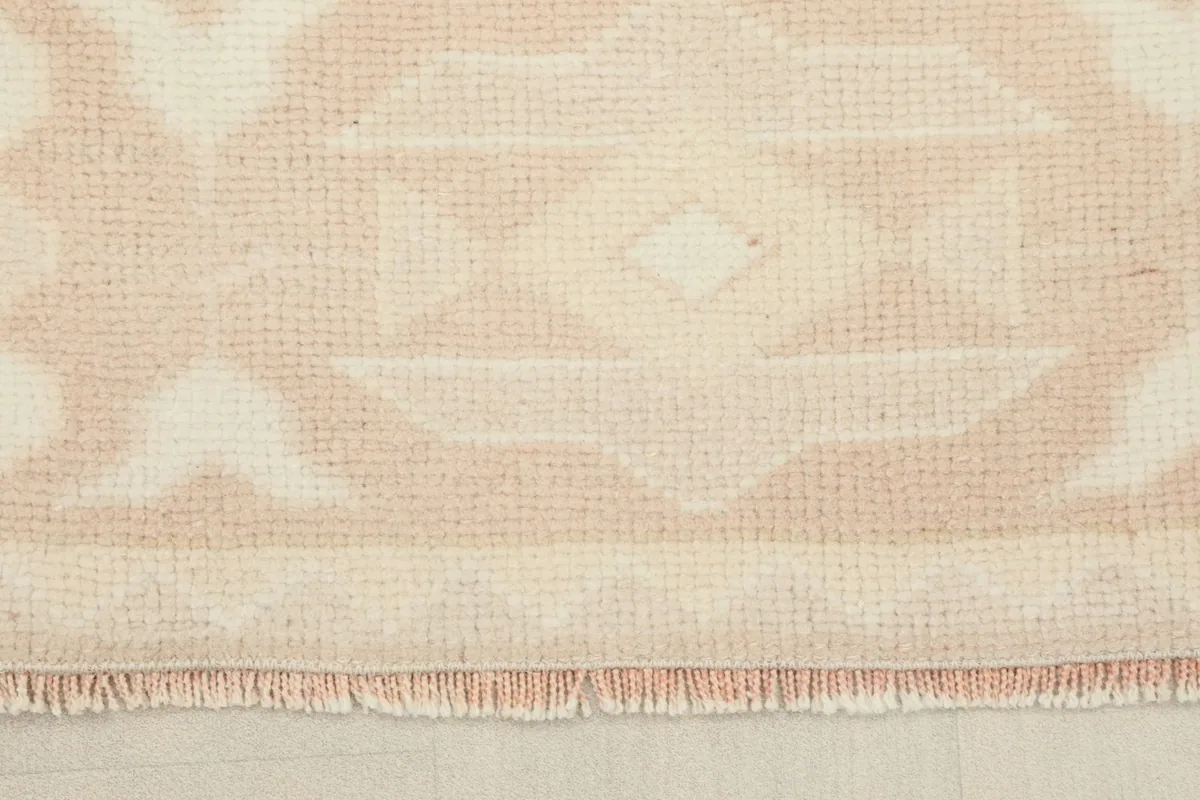 Close-up view of the rug's short, natural fringes and the edge of the low wool pile.