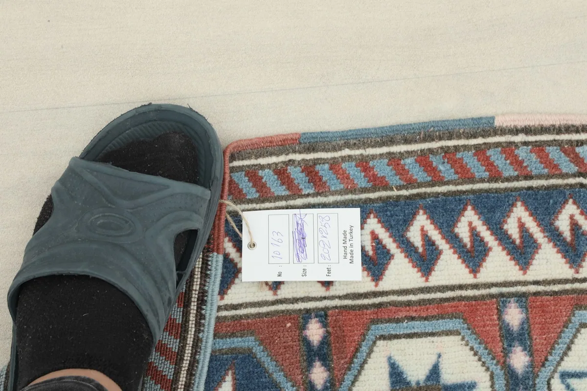 Extreme close-up of the rug's low pile, with a slipper for scale, showing the texture and tag