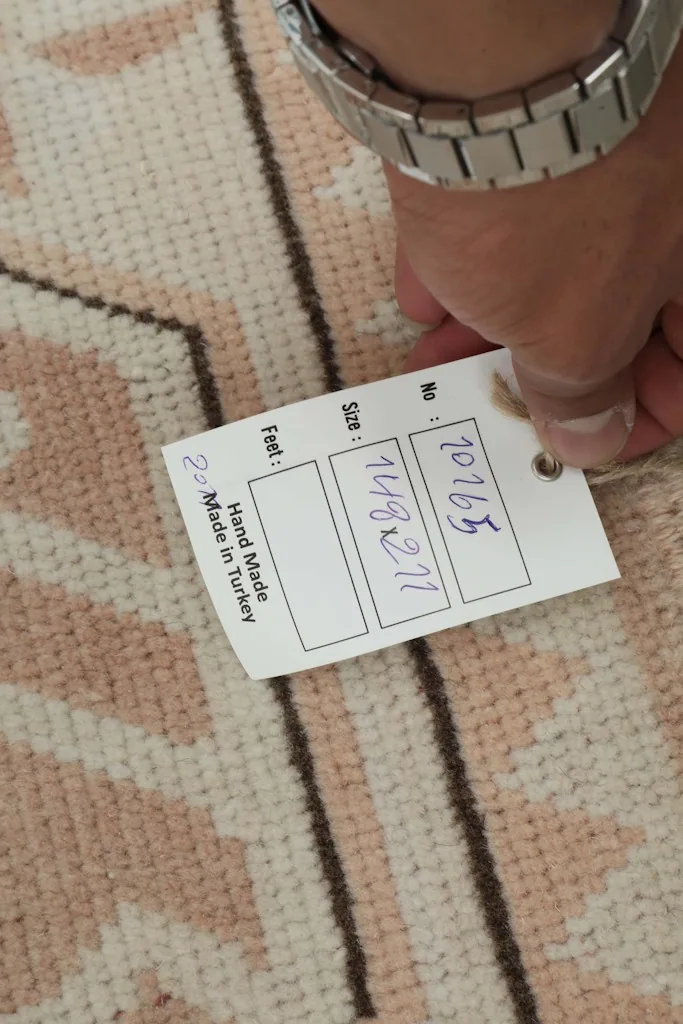 Hand holding a tag showing the rug's dimensions and 'Hand Made in Turkey' details.