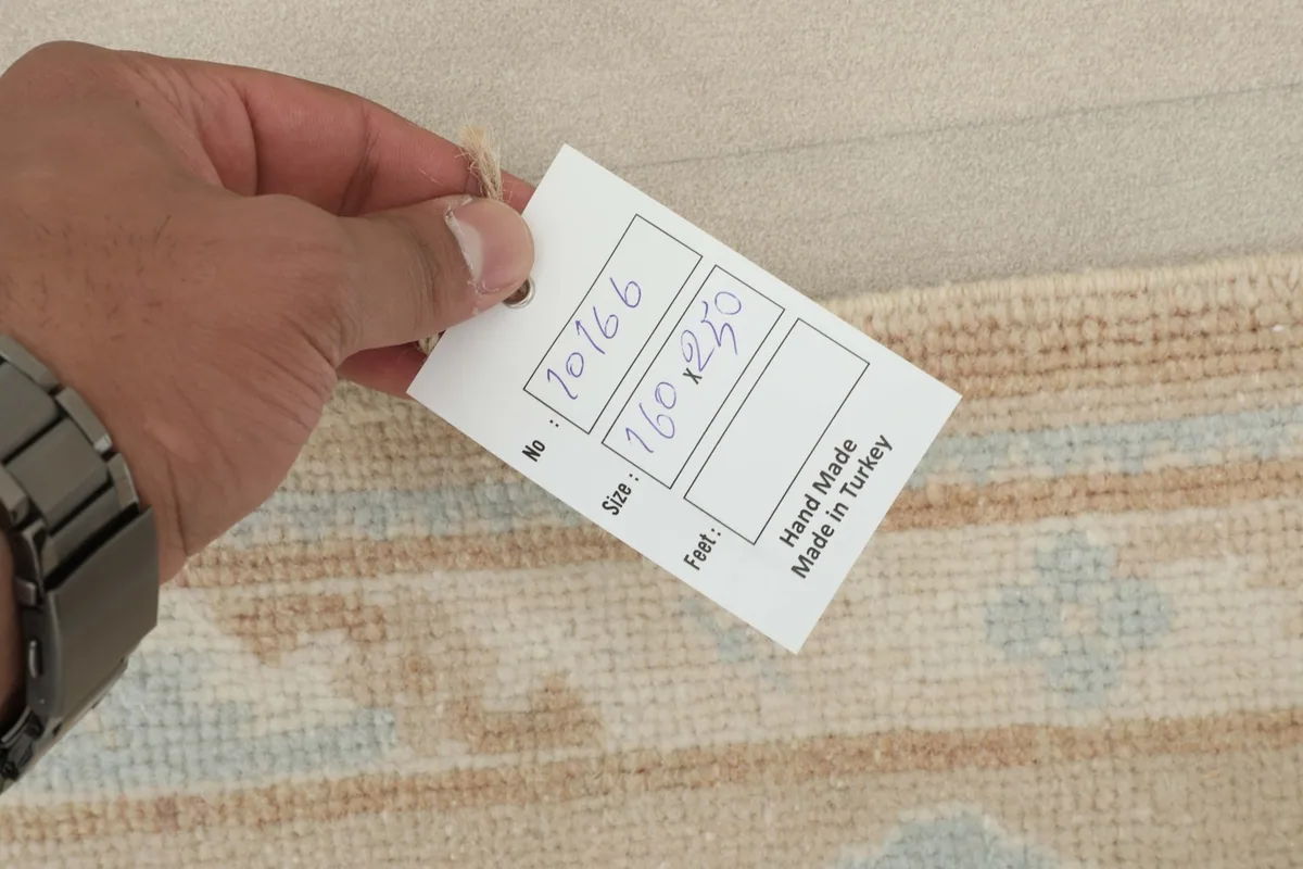 Hand holding a tag showing the rug's item number and size in centimeters, 'Hand Made in Turkey'.