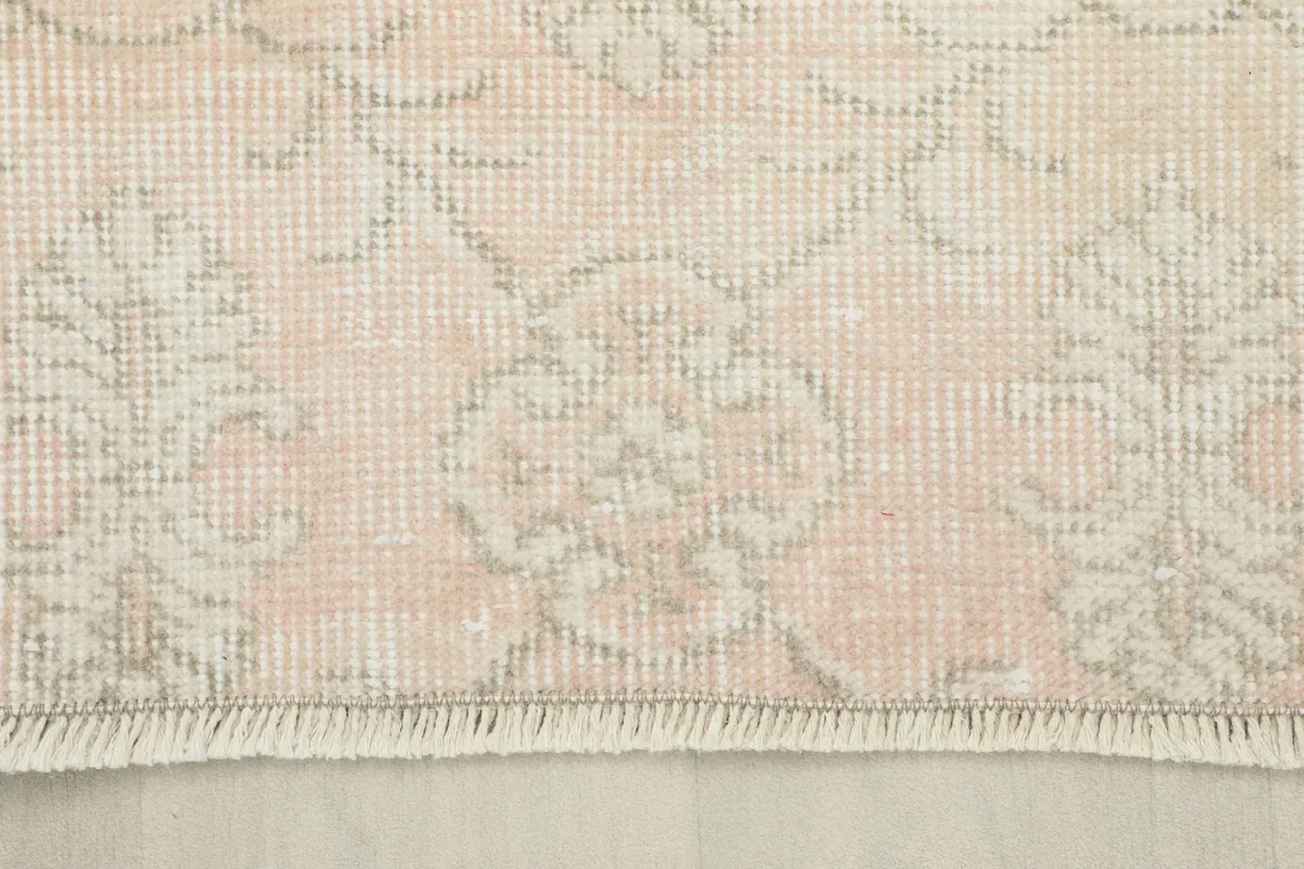 Close-up of the rug's edge, showing the faded rose color and the short, simple fringe.