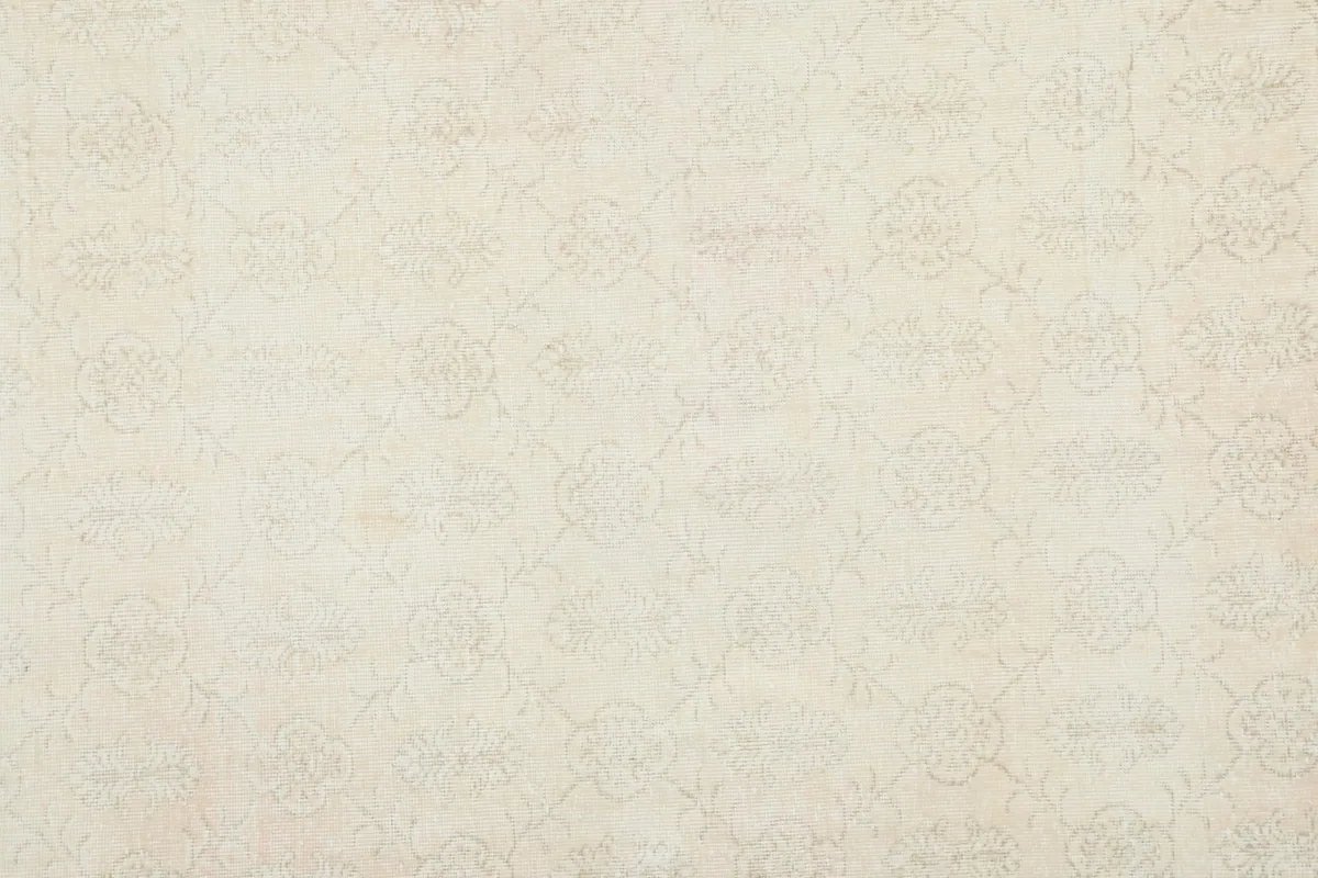 Close overhead view of the rug's cream field with its repeating, faded floral pattern.