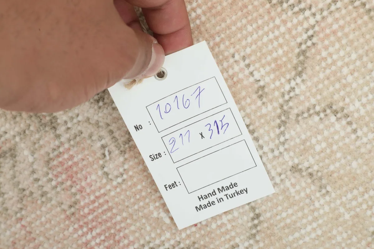 Hand holding a tag showing the rug's inventory number and its dimensions in centimeters.