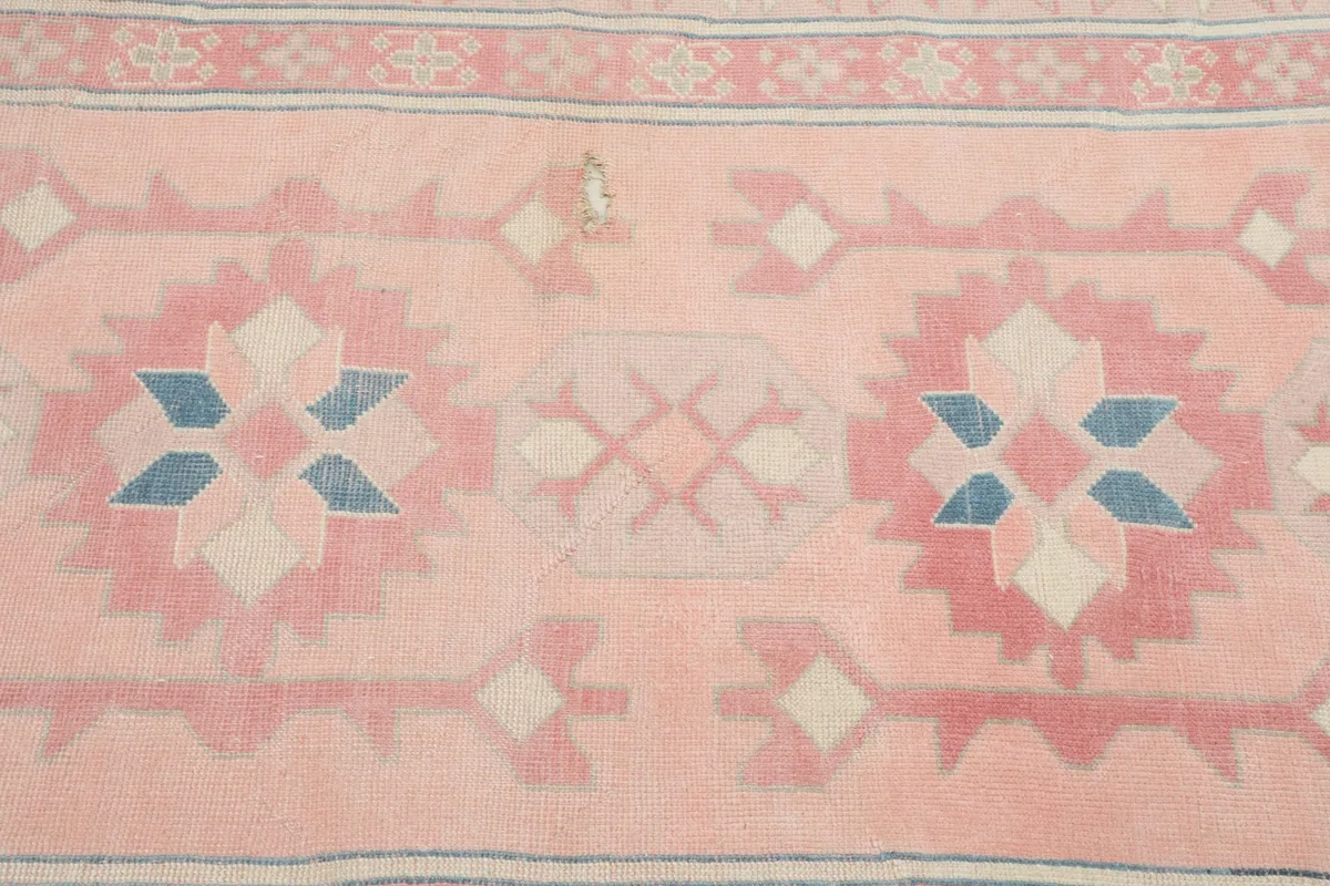 Detailed view of the central geometric motifs in pink, blue, and ivory with slight wear