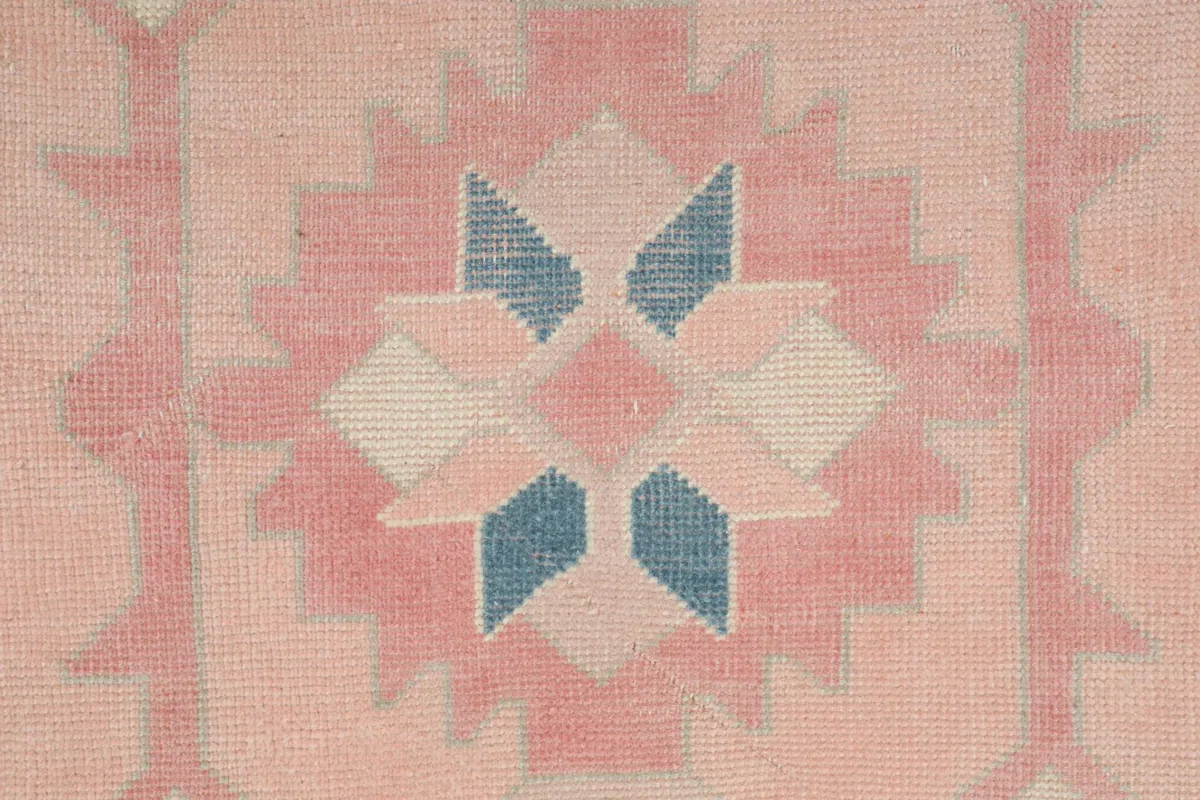 Close-up of a central geometric medallion with blue and pink elements, showing wool texture