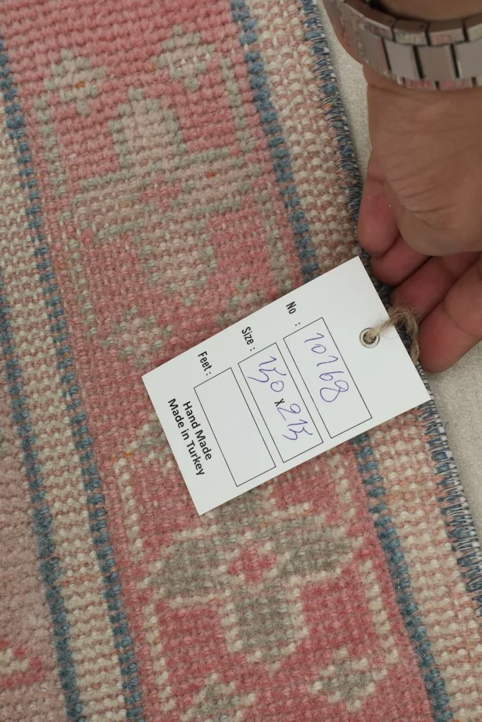 Hand holding a tag showing the dimensions 151x215 cm and 'Hand Made in Turkey'