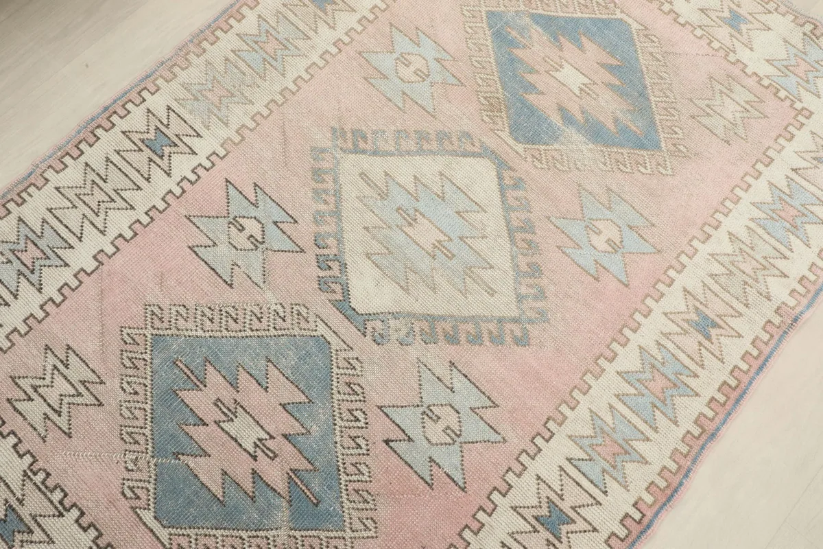 Detailed view of the central diamond motifs in blue and ivory against the pink background