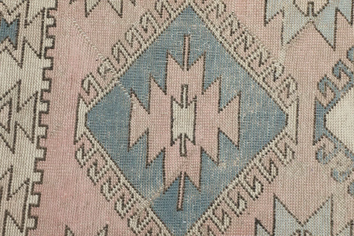Extreme close-up of a blue geometric diamond motif, showing the hand-knotted wool texture