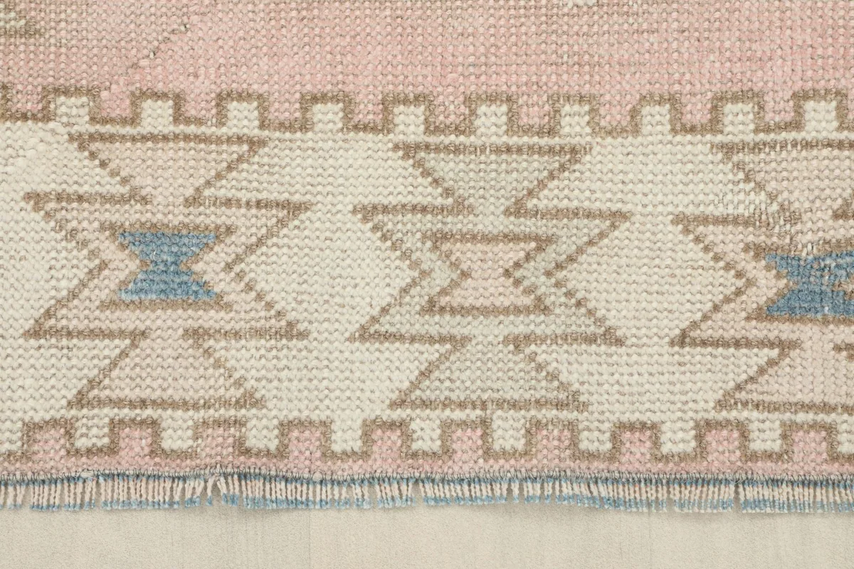 Close-up of the rug's border with ivory geometric patterns and short, hand-finished fringe