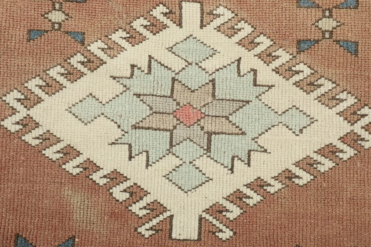 Detailed view of one central geometric medallion in cream, blue, and pink on the rust field
