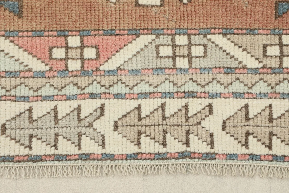 Detailed view of the rug's border showing a sequence of stylized motifs and fringe