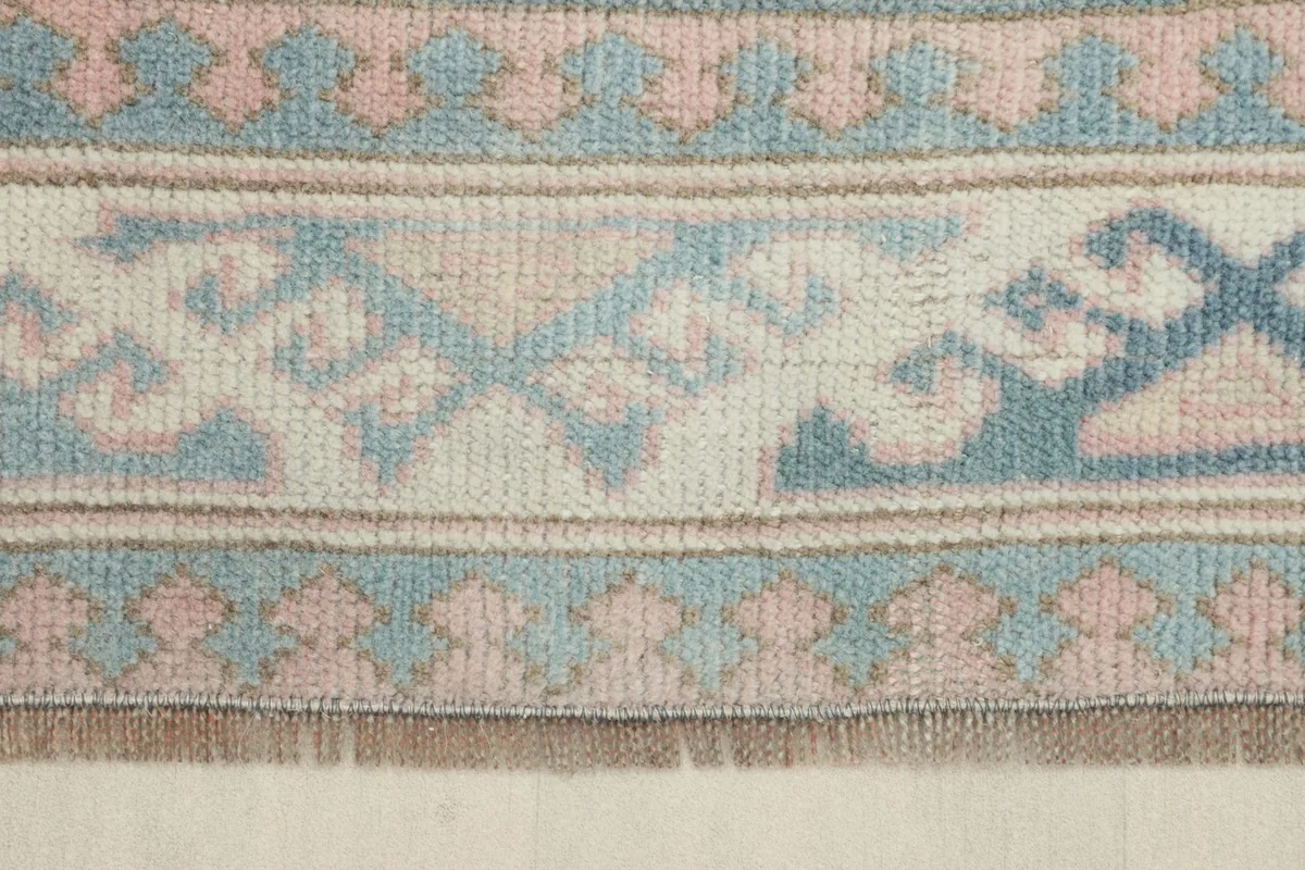 Close-up detail of the rug's border, showing faded rose and blue geometric motifs and low pile.