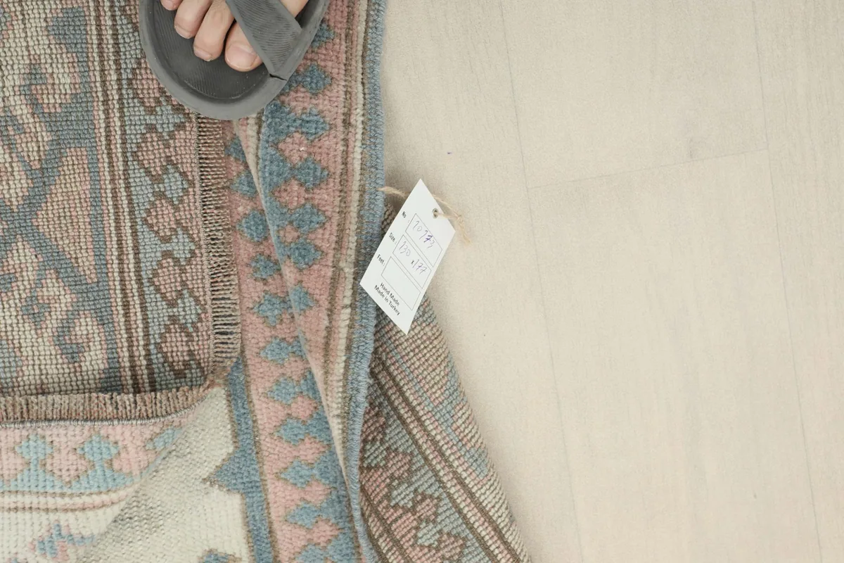 A foot in a sandal next to the rug, showing scale and the RugsKilim tag on the reverse side.