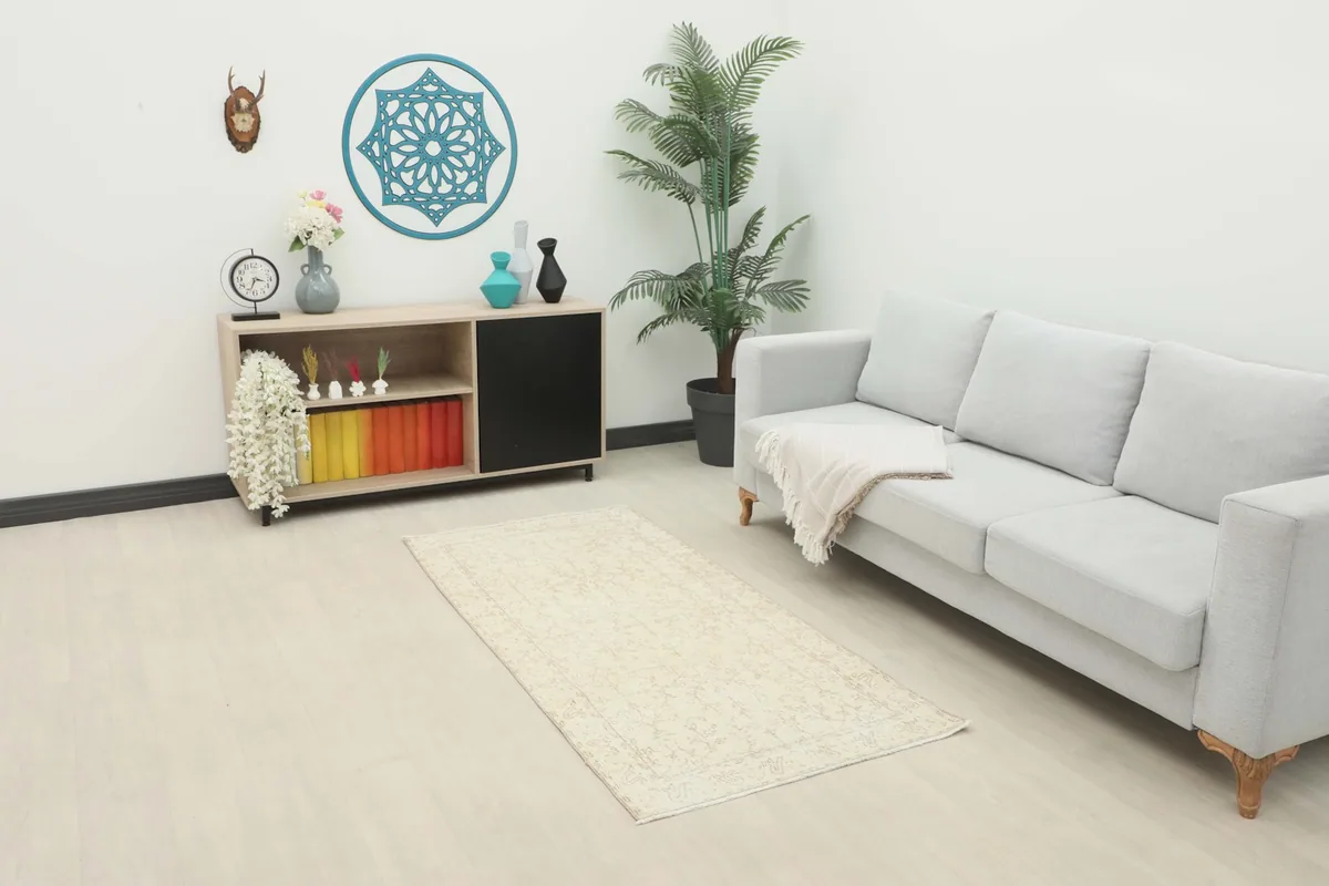 Soft ivory and beige floral vintage rug placed in a modern living room setting with a light gray sofa and wooden cabinet.