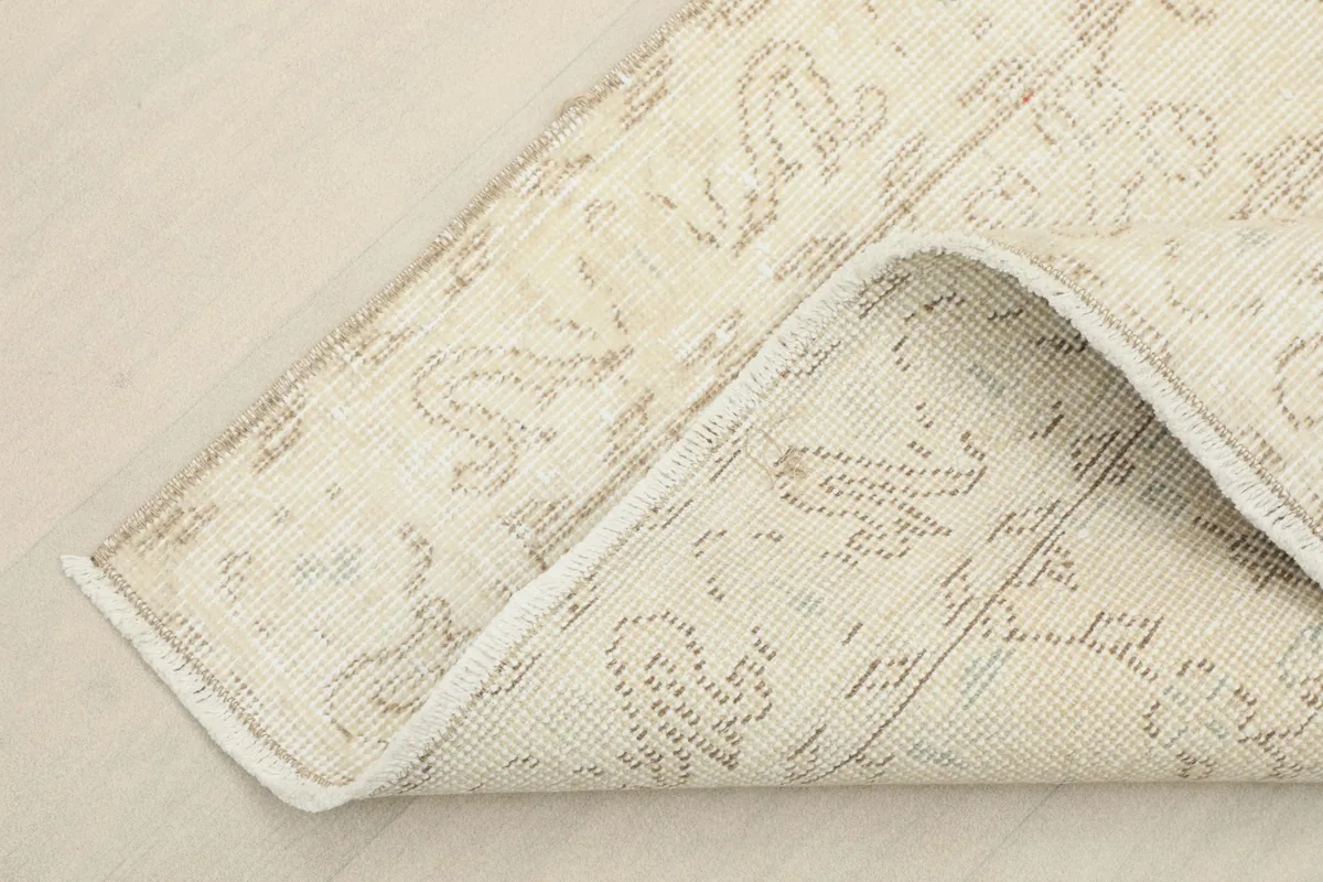 Corner of the rug folded back, showing the cotton foundation and the reverse side of the hand-knotted construction.