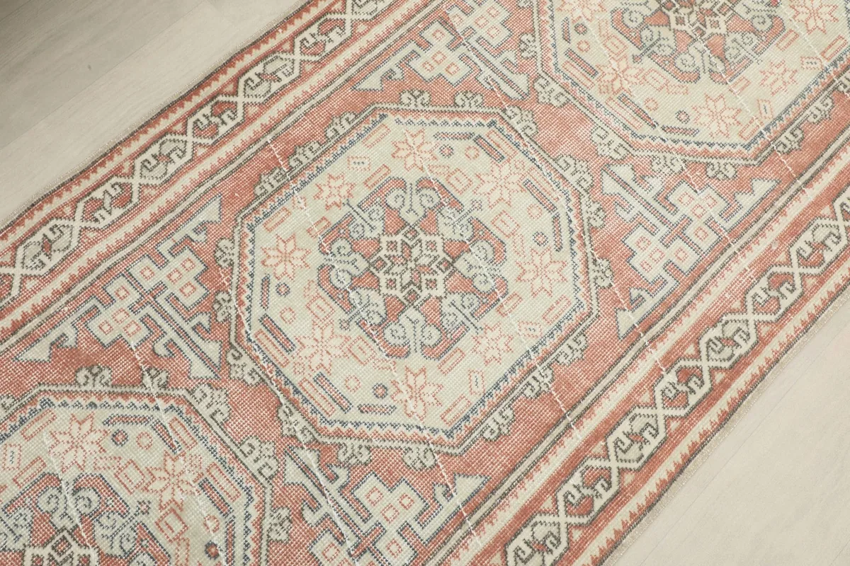 Close-up showing the repeating medallion design and the surrounding geometric field in rose, ivory, and gray