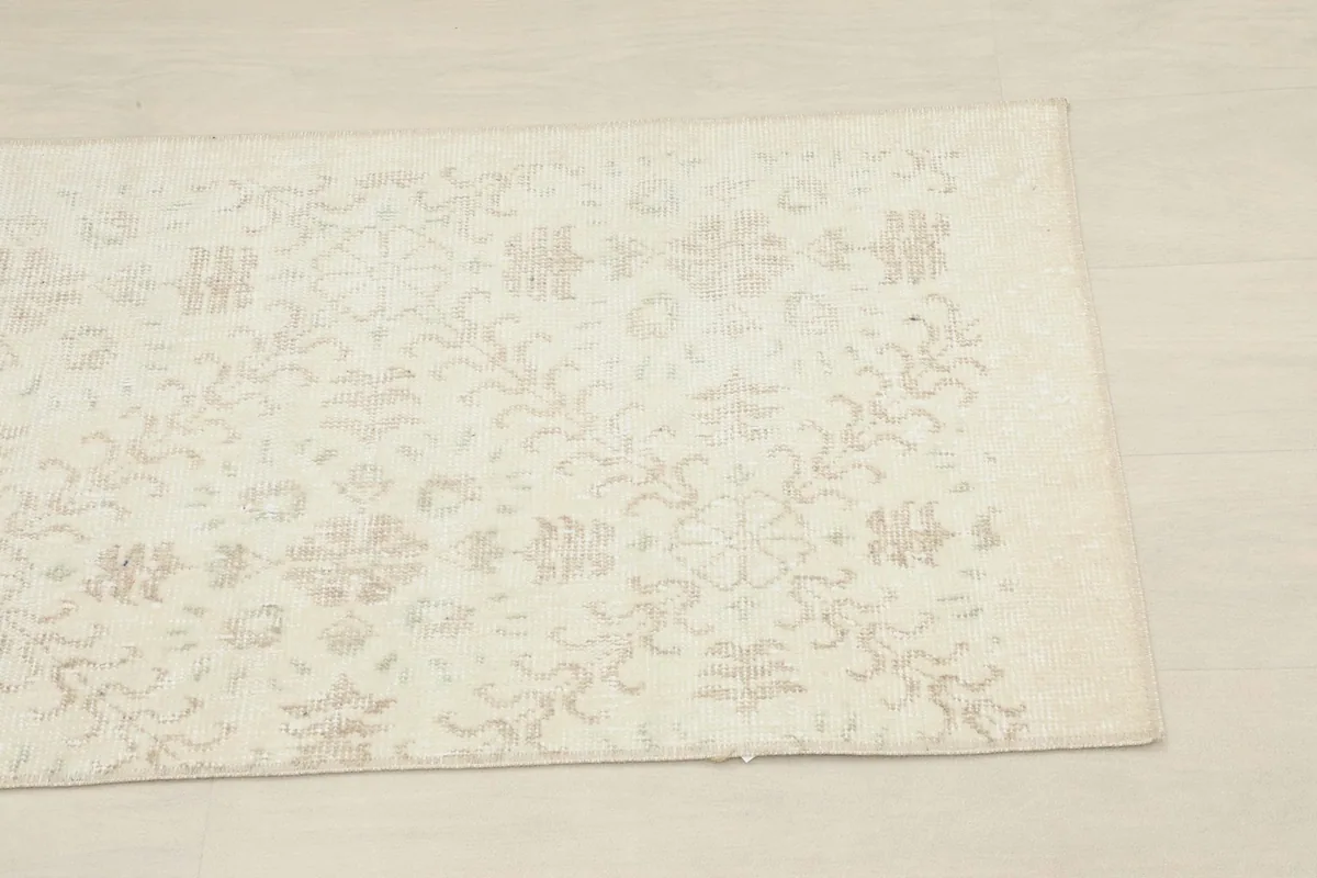 Close-up of one end of the ivory and beige runner, highlighting the faded floral and geometric patterns.