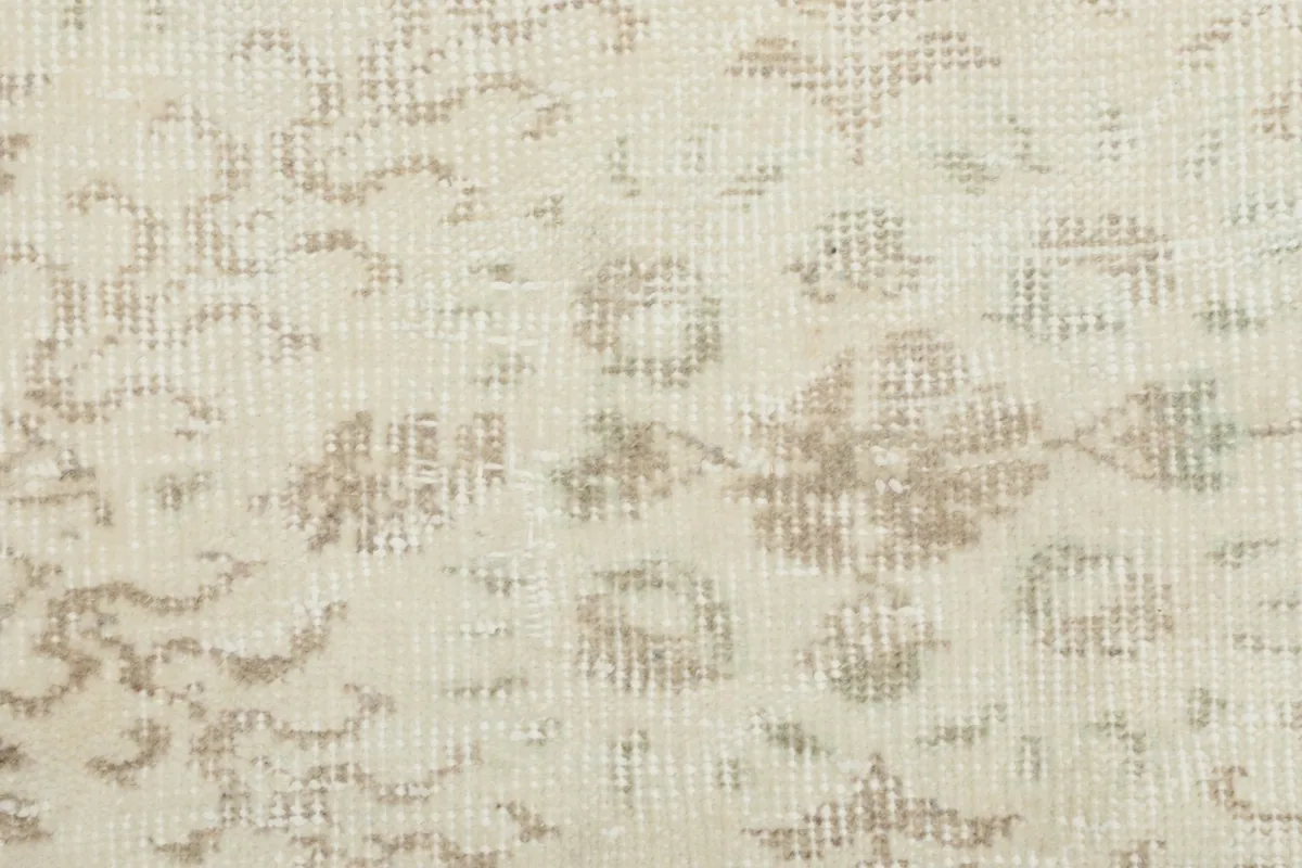 Detailed close-up of the low wool pile and faded beige patterns on the ivory background.
