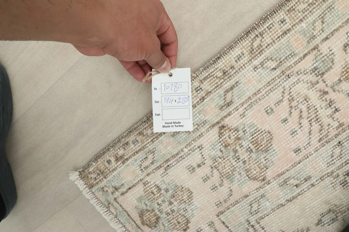 Hand holding a tag indicating 'Hand Made in Turkey' and other rug details, over the rug's surface.