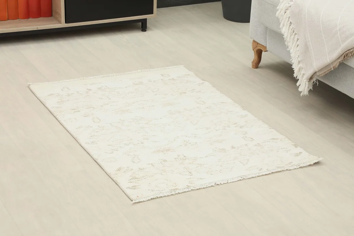 Angled view of the mini ivory and beige rug on a light-colored floor, showing its placement relative to furniture.