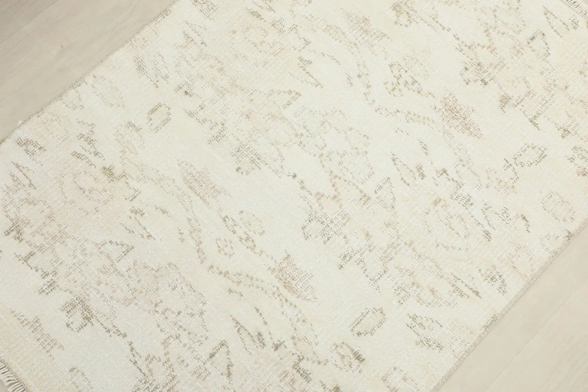 Diagonal view across the rug surface, emphasizing the overall faded appearance and beige tribal motifs.