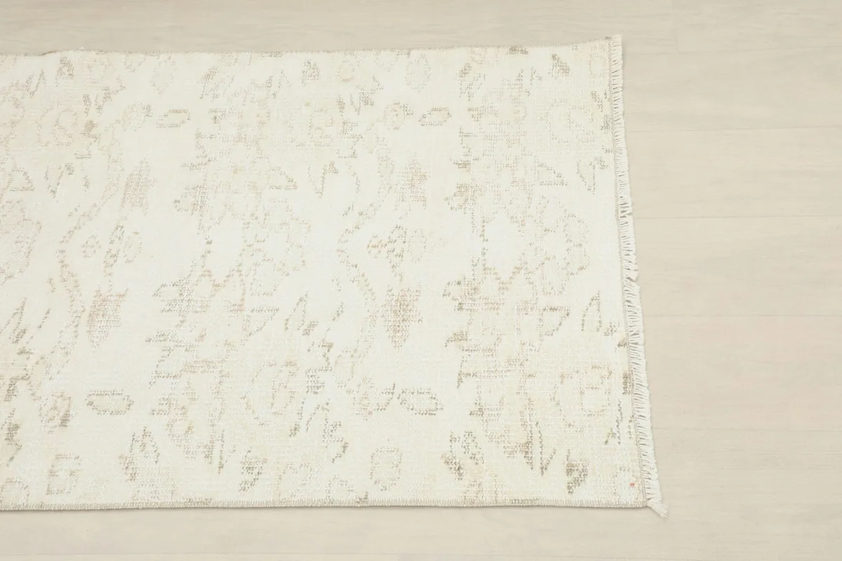 Close overhead shot of one corner of the rug, highlighting the faded geometric patterns and ivory color.
