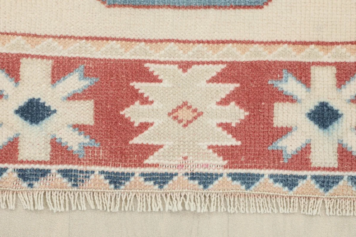 Detail of the rug's red border with white and blue starburst-like patterns and fringe