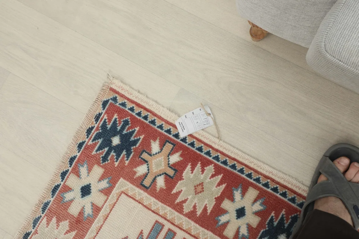 Overhead view of a corner of the rug with a small tag and a foot for scale