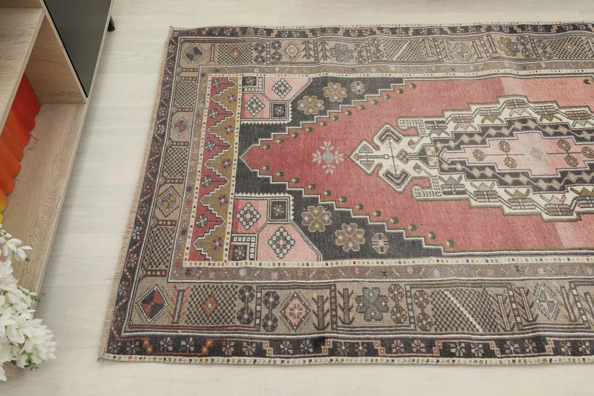Detailed angle view highlighting the faded rose field and charcoal border of the vintage Anatolian rug.
