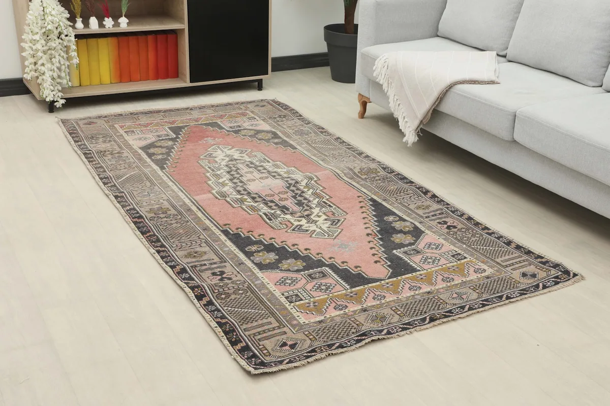 Angle view of the rose and charcoal geometric rug placed under a sofa in a contemporary space.