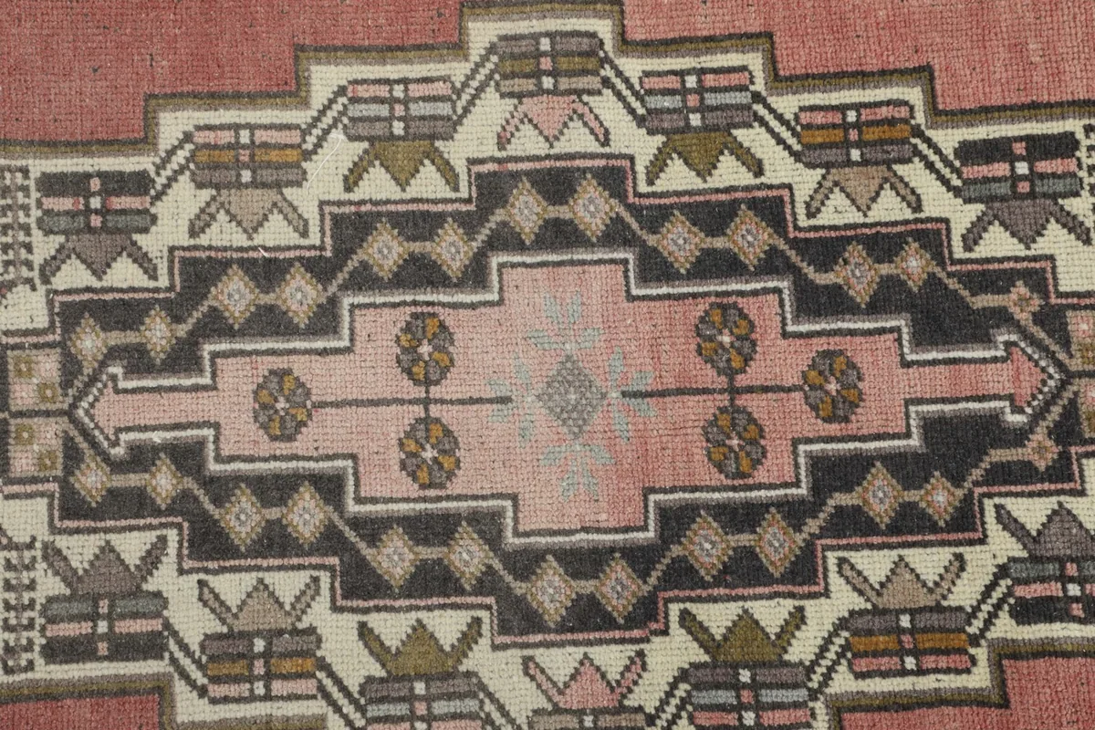 Close-up detail of the central medallion's intricate geometric and tribal motifs in charcoal, ivory, and rose.