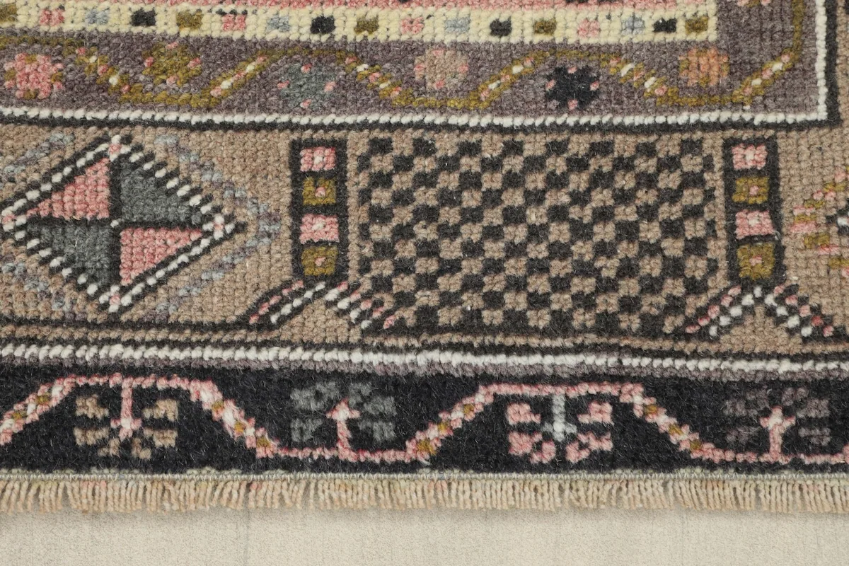 Detail of the rug's border, showing small geometric patterns and the blend of charcoal, tan, and pink threads.