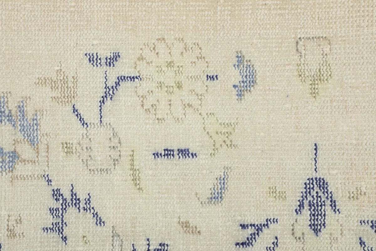 Detailed view of the hand-knotted floral patterns in blue and green against the ivory wool pile.