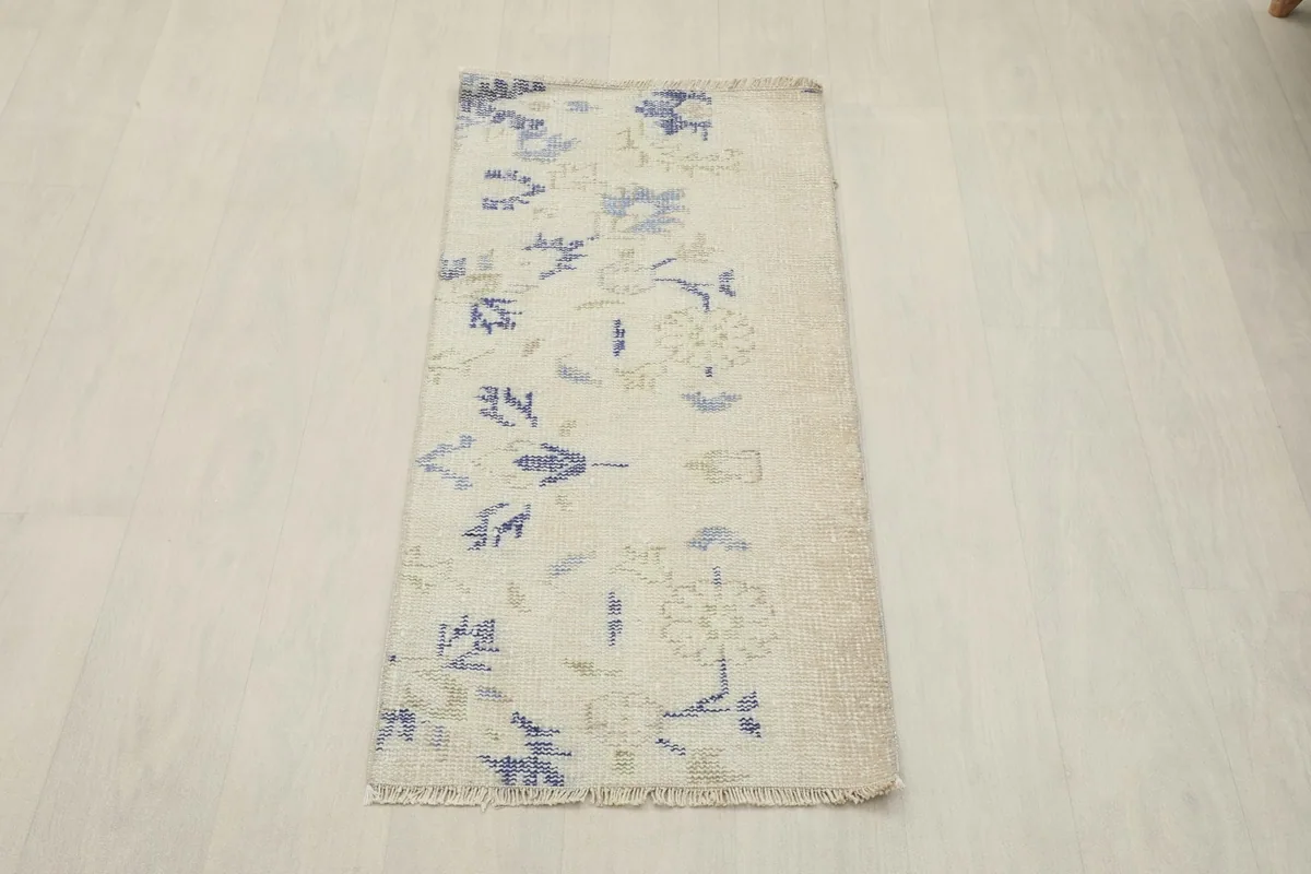 Full overhead view of the ivory rug with blue and green patterns, laid flat on a light wood floor.