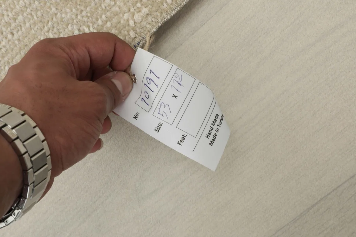 Hand holding a tag showing the rug's dimensions (53 x 112 cm) and 'Hand Made in Turkey'.