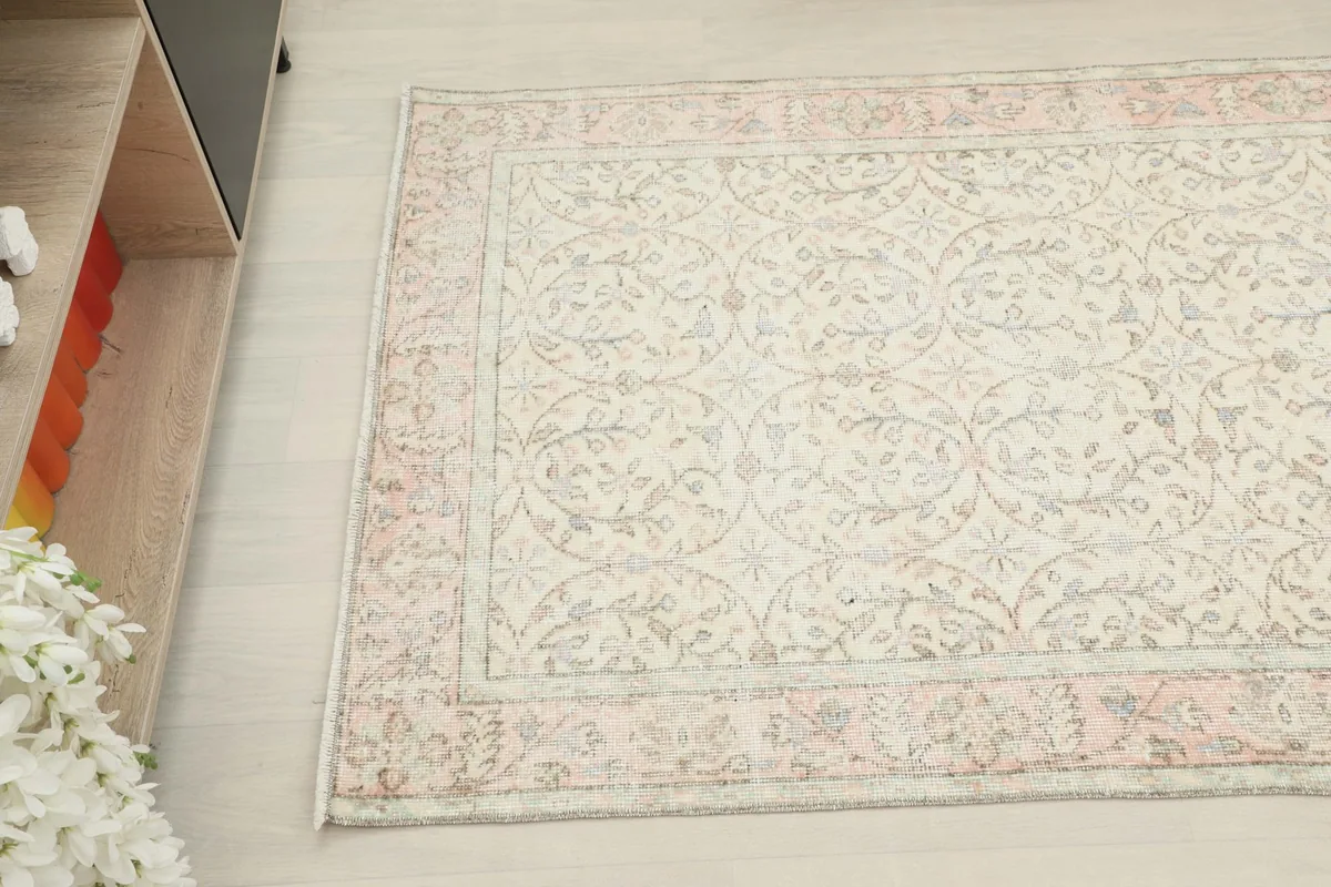 Overhead angled view of the rug, capturing the subtle floral motifs in the ivory field and the pink border.