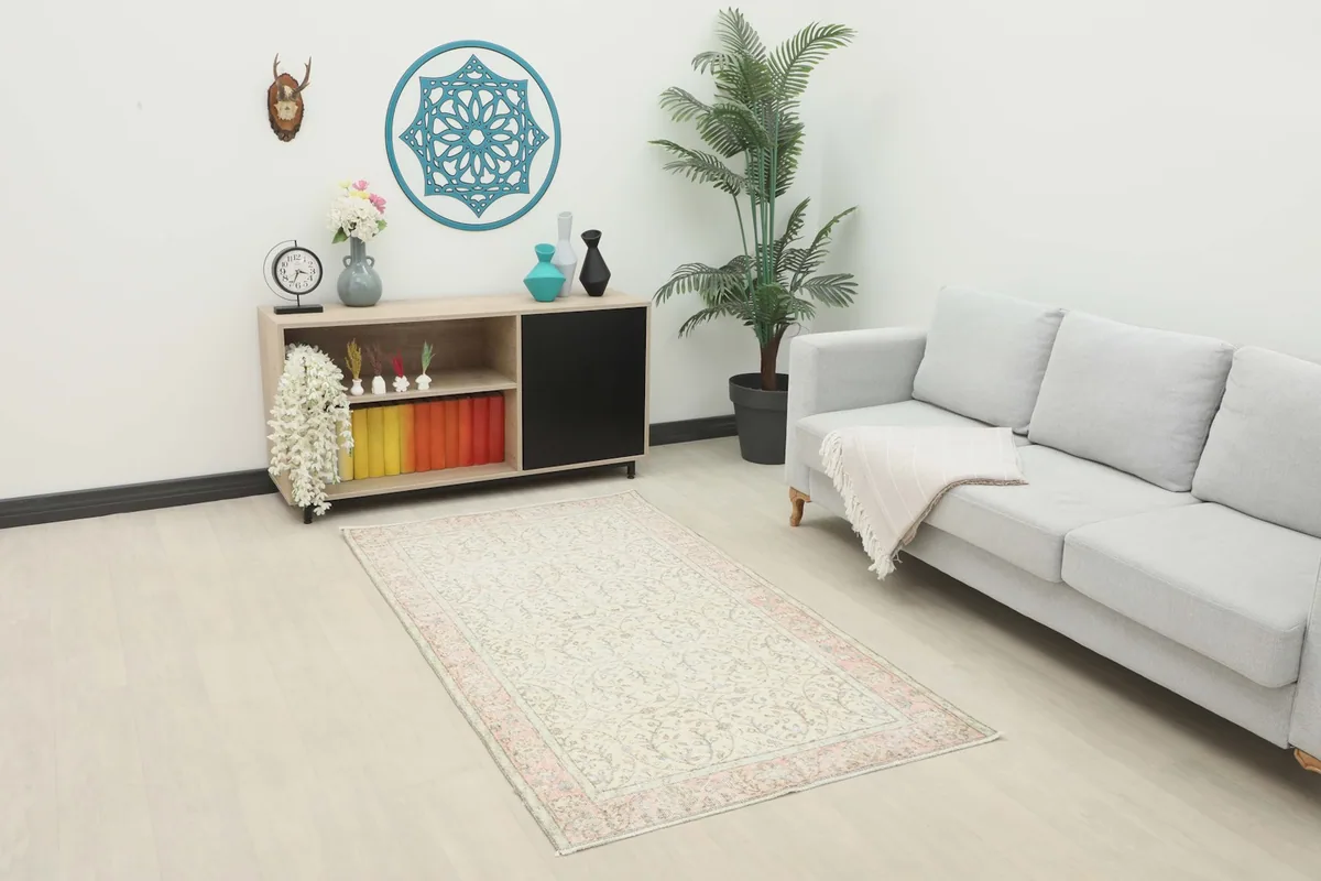 Ivory and pink vintage rug styled in a modern living room setting with a gray couch and wooden cabinet.