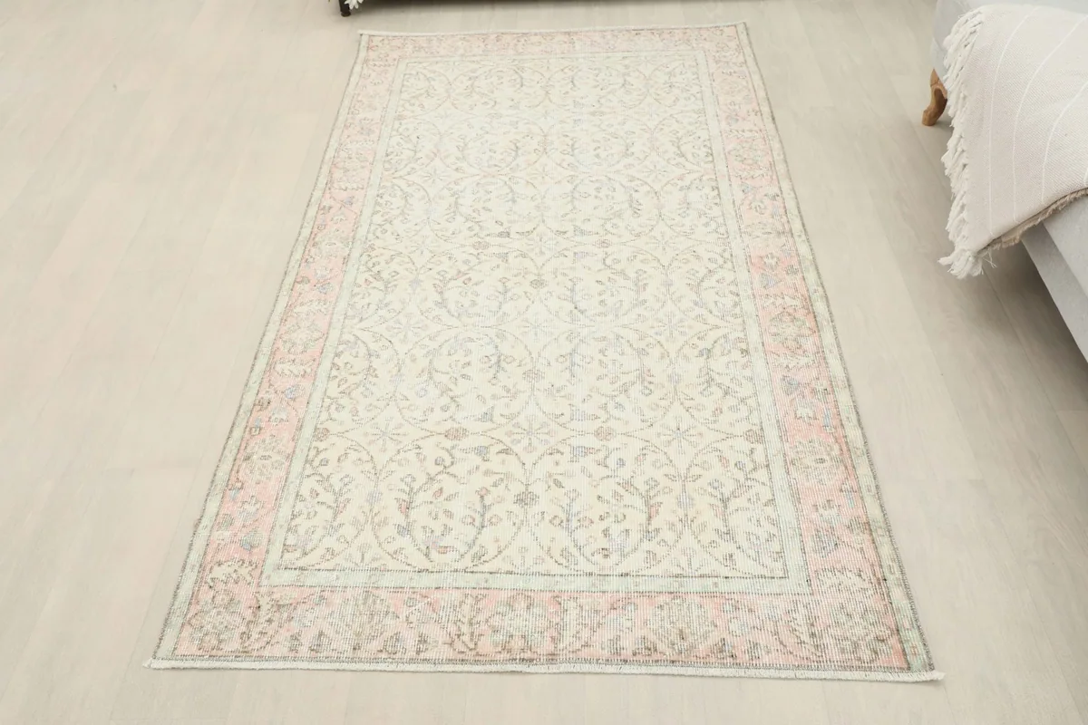 Full room view of the ivory and pink vintage rug, positioned in a clean, bright interior space.