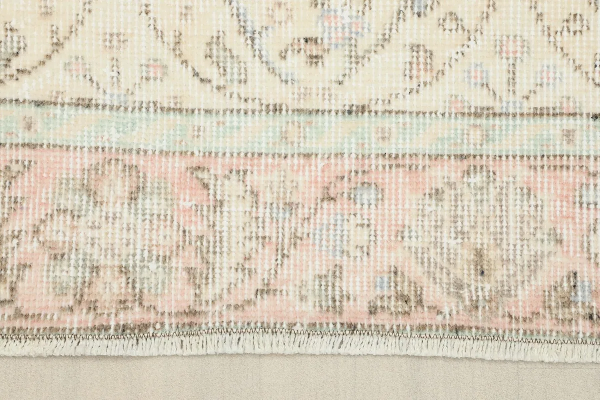 Close-up of the rug's border, highlighting the pink and gray tones and the subtle wear on the fringe.
