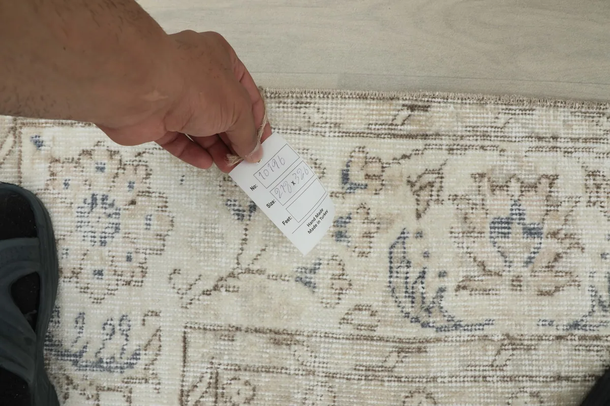 Hand holding a tag over the rug, showing the texture and pattern detail