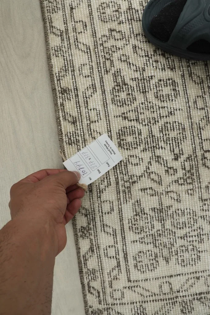 Hand holding a size tag near the rug's edge, highlighting the weave and pattern.
