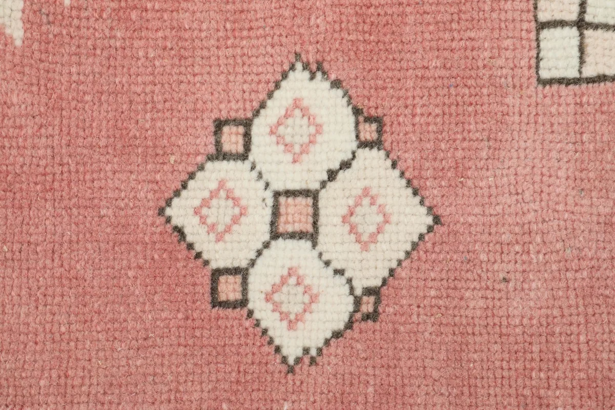 Detailed view of a small geometric motif in rose and ivory on the rug's field