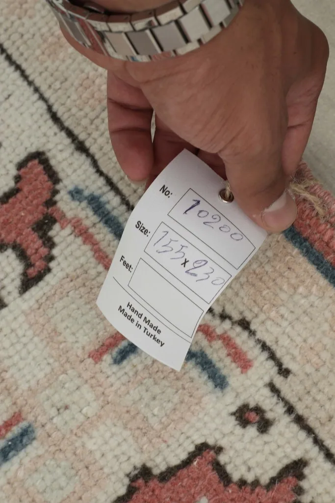 Hand holding a tag showing the rug's size in centimeters and 'Hand Made in Turkey'