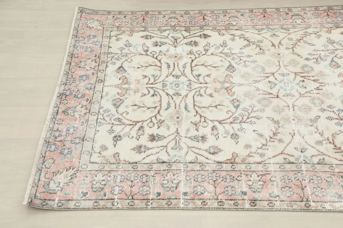 Close-up detail of the top left corner of the ivory rug, showing the blend of rose, blue, and brown colors.