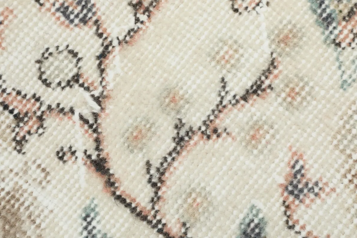 Macro shot of the hand-knotted wool pile and intricate floral design in muted colors.