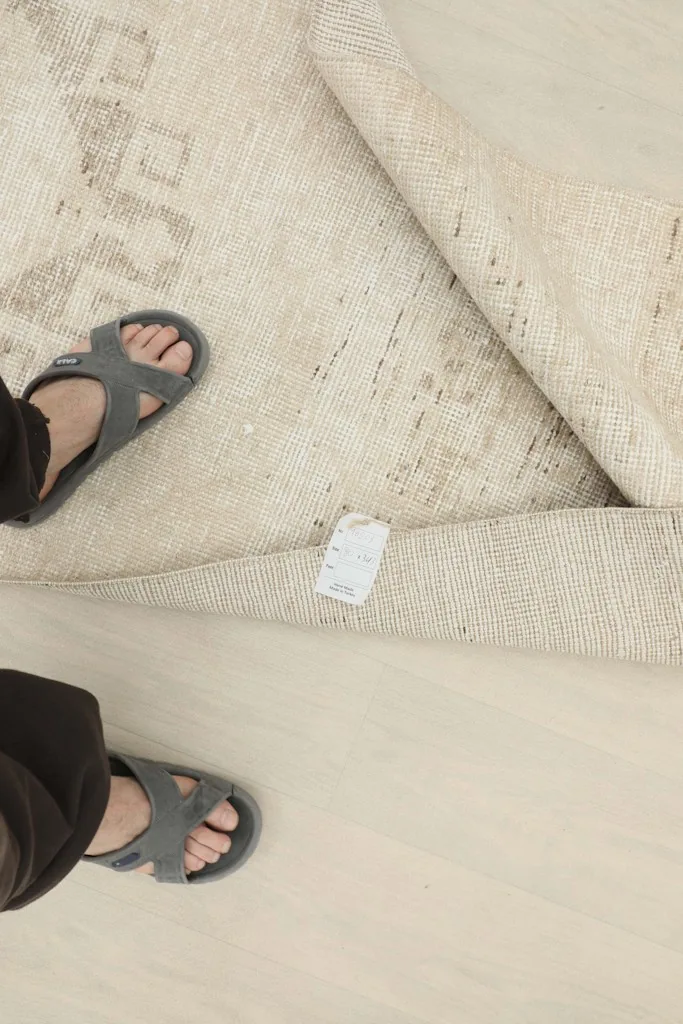 Overhead view of the rug with feet for scale, showing the tag and the hand-knotted construction.